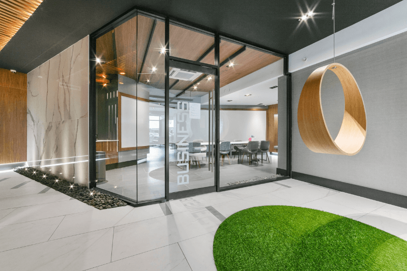 A modern office lobby with a glass wall and a green grass area.